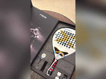 مضارب التنس / بادل أزرق-أبيض للكبار 19 بوصة Nox AT10 Pack Luxury Genius 18K Alum Aires ExclusiveEdition 25 76.9 بوصة للمتقدم